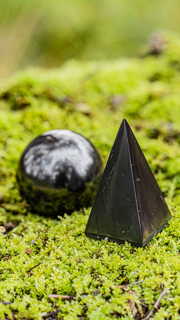 Shungite pyramid and sphere on a mossy forest floor, natural healing stones